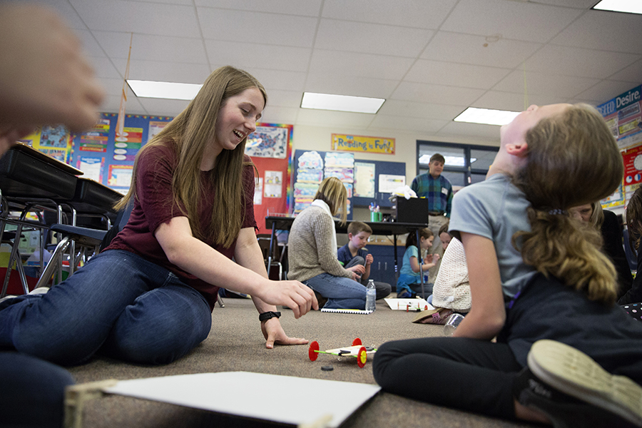 A student teacher sits on the floor with a young student as they build a pretend car.