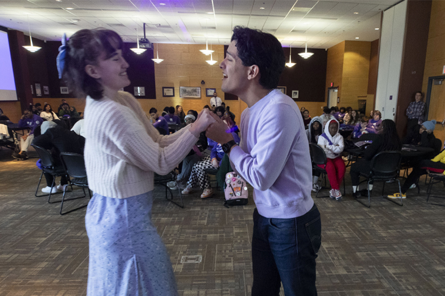 Two people hold each other's hands as they perform in front a group of people.