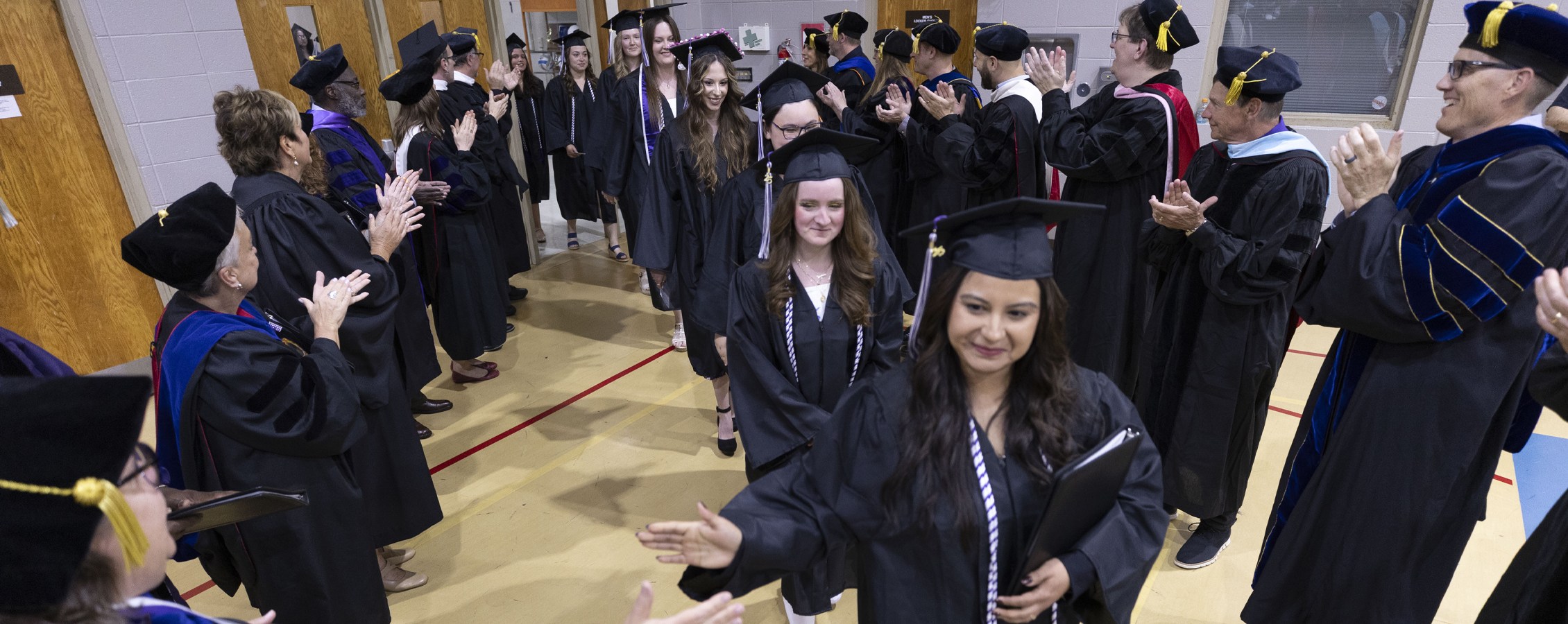 Students wearing graduation regalia celebrate indoors on the Rock County campus.