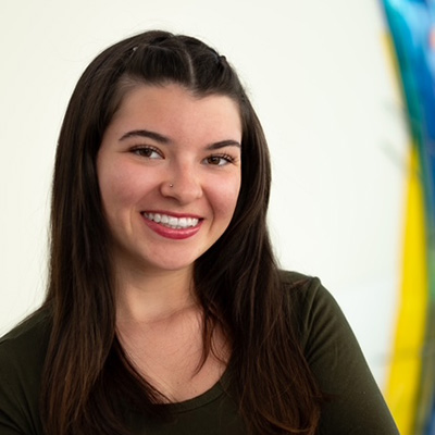 Breanna Flores wearing a black shirt in front of a white, blue, and yellow background.