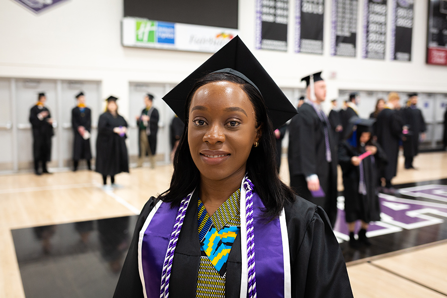 An international student is dressed in academic regalia and smiles at the camera.