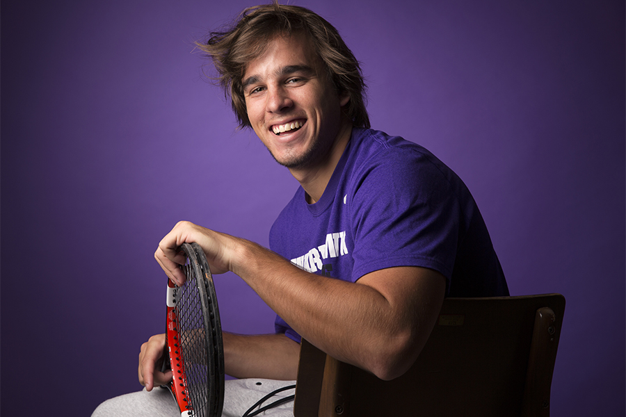 Lucas Monterros smiles at the camera and holds a tennis racket. 