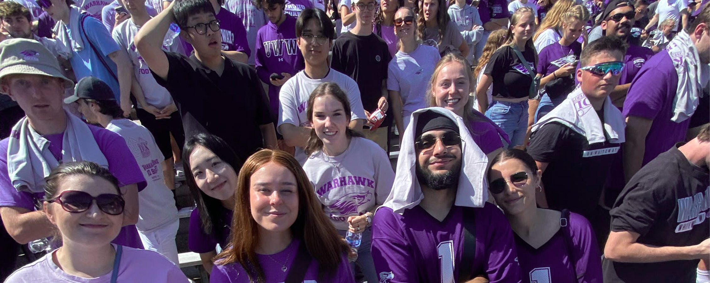 A group of international students pose for a photo while in the stands at Perkins Stadium watching a football game.