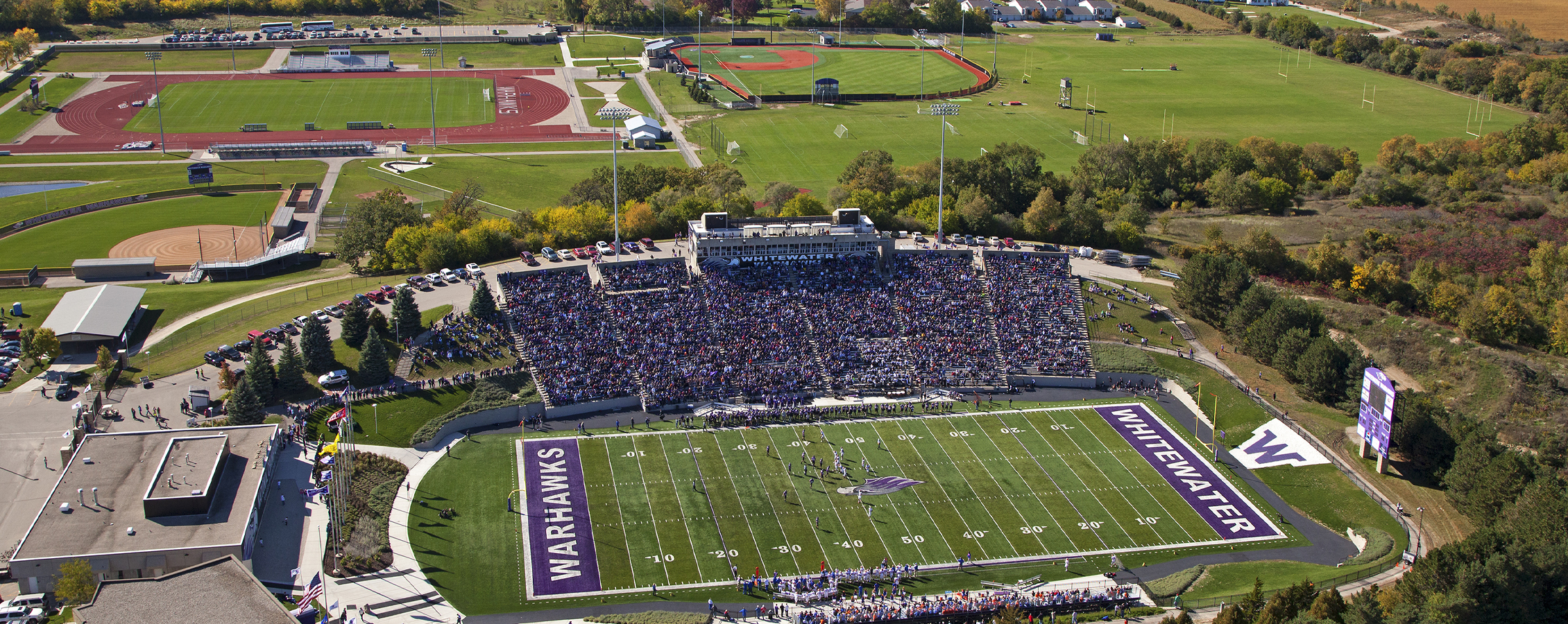 An aerial view of the football stadium, baseball diamond and track area surrounded by large trees.