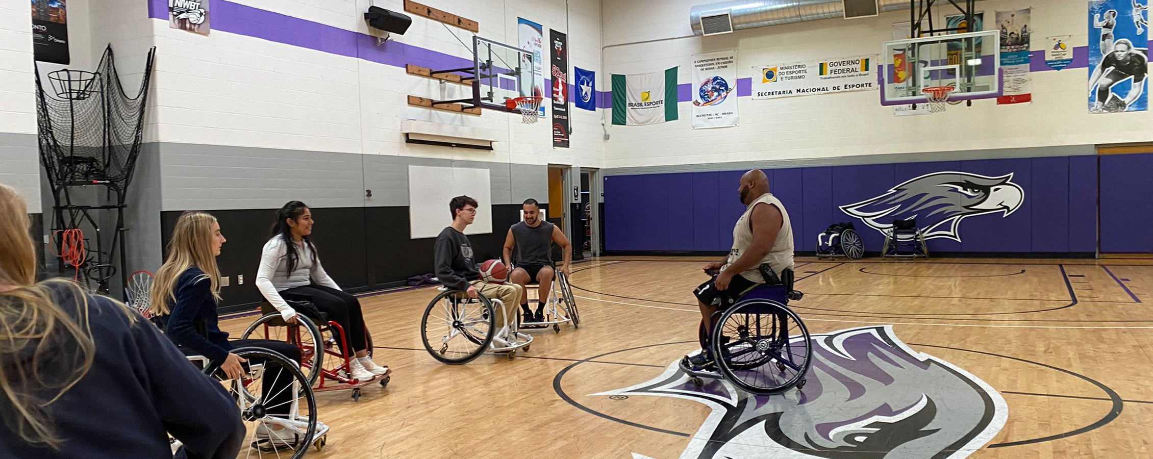 An international student from Sweden coaches wheelchair basketball in a gym.