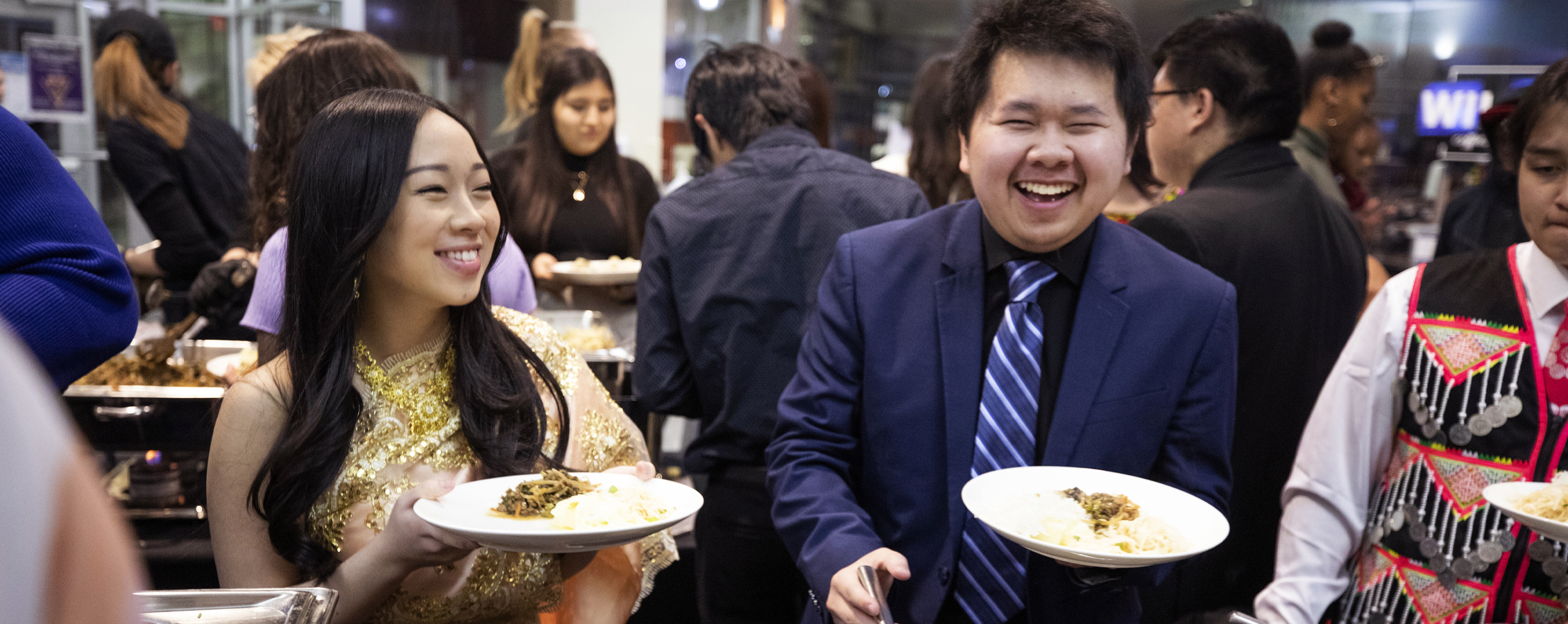 Two international students laugh together as they get food from a buffet.