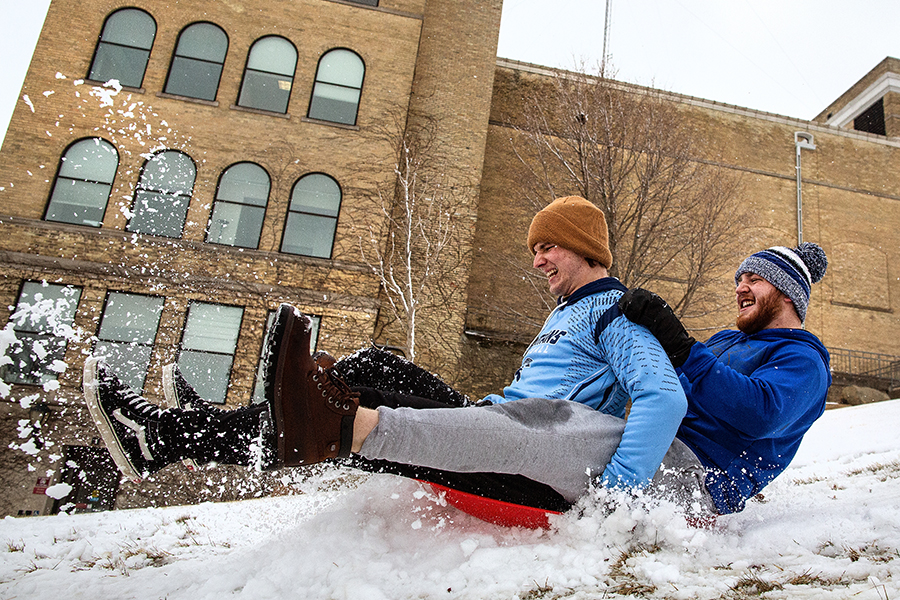 Two people sled down a snowy hill by Hyer Hall.