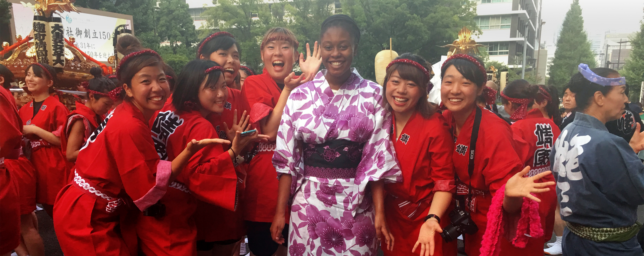An African American female stands in a crowd of smiling people in Japan.