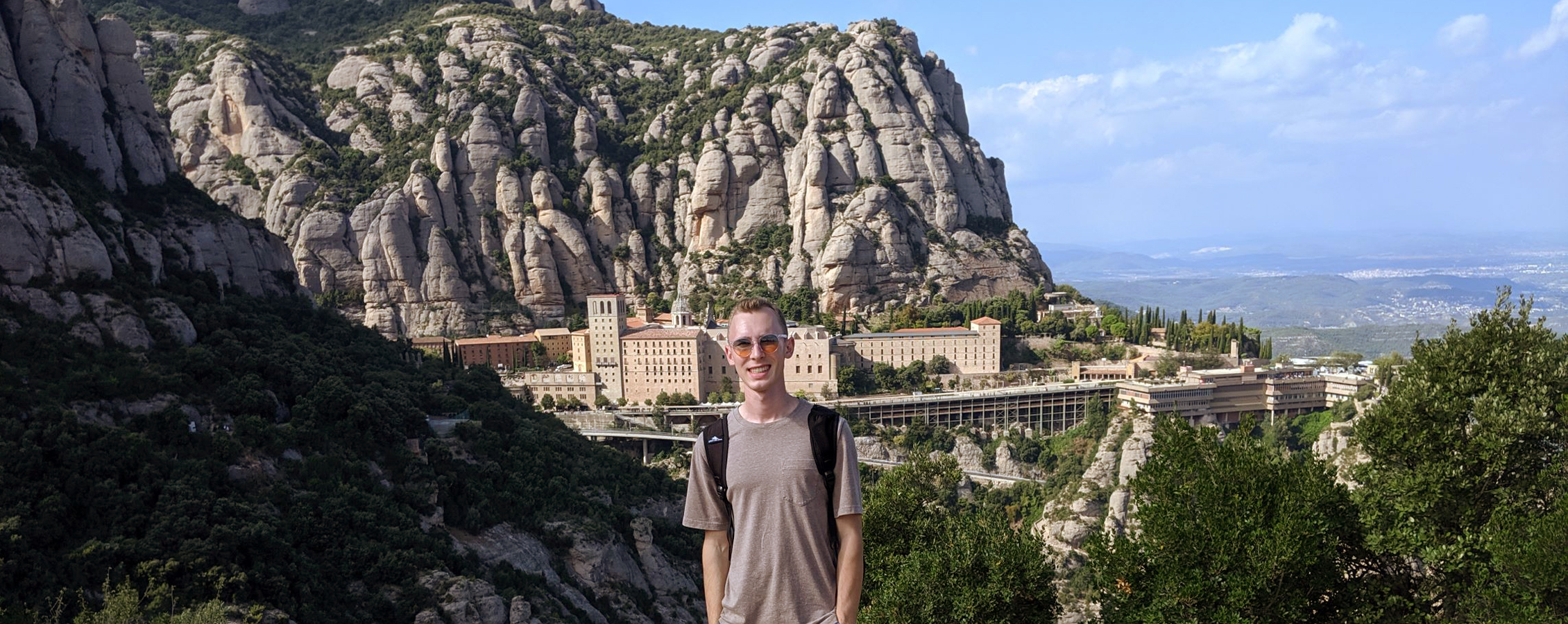 A person poses for a picture in front of a city built into a large mountain.