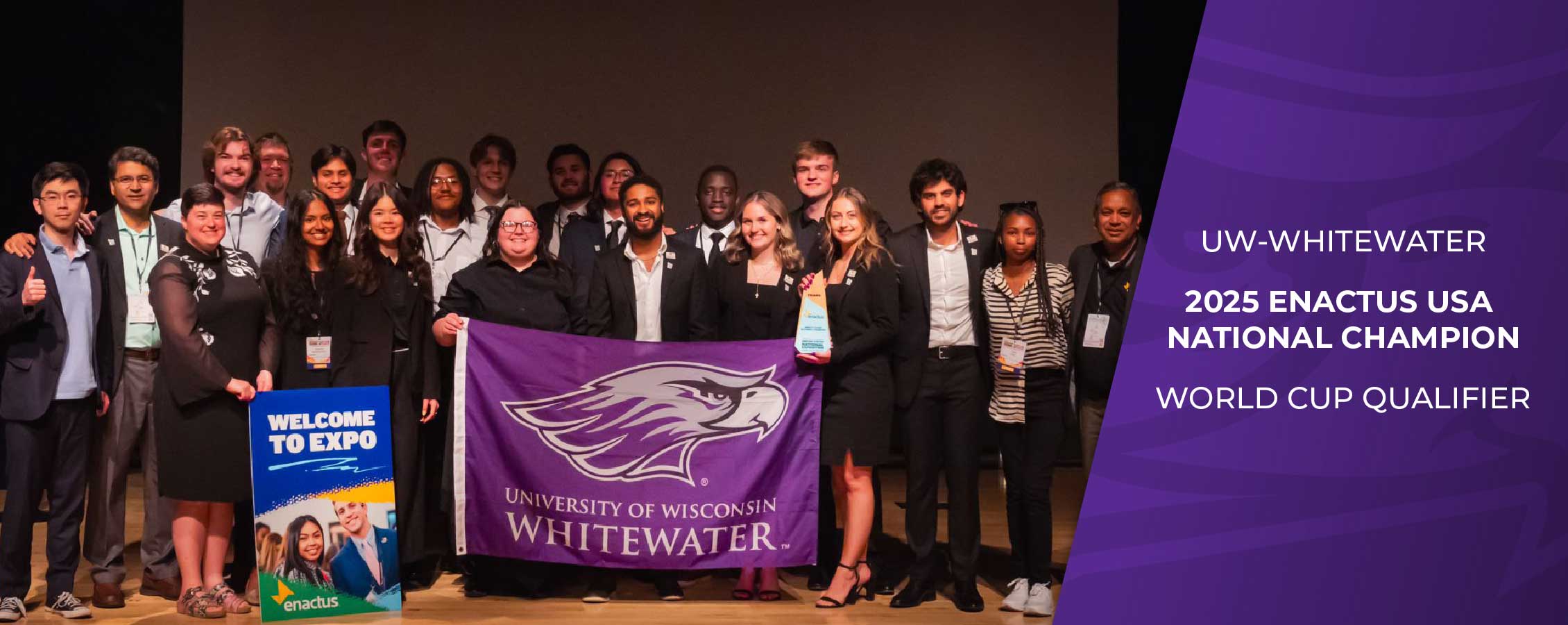 A large group of students pose for a photo while holding a purple UW-Whitewater flag.