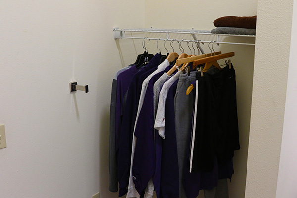 A closet. There is a wire shelf with clothes hanging on it, and a towel rack.