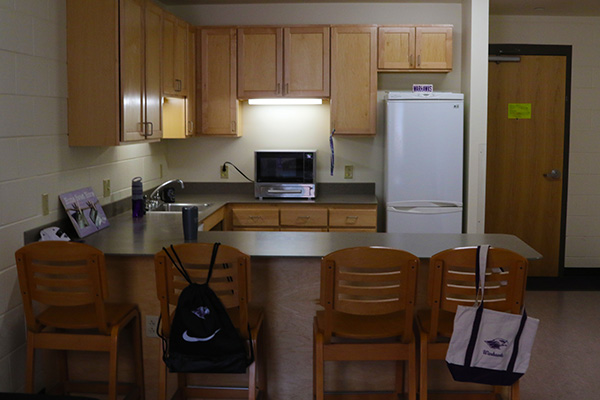 A kitchen with many cabinets, a fridge, a combined toaster oven and microwave, and a breakfast bar.