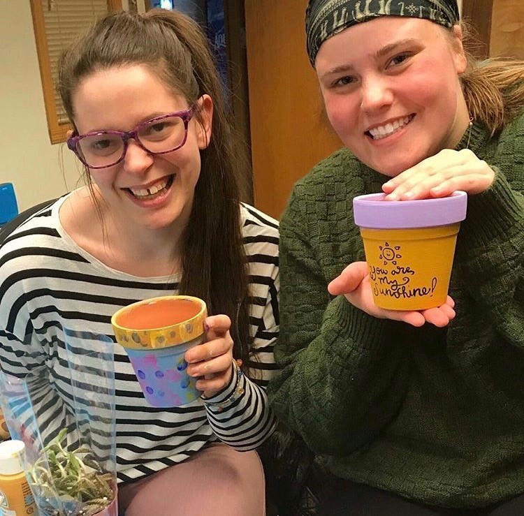 Two residents holding painted garden pots at a sustainability program