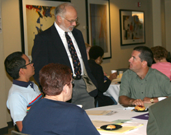 A man standing, talking to a group sitting at a table.