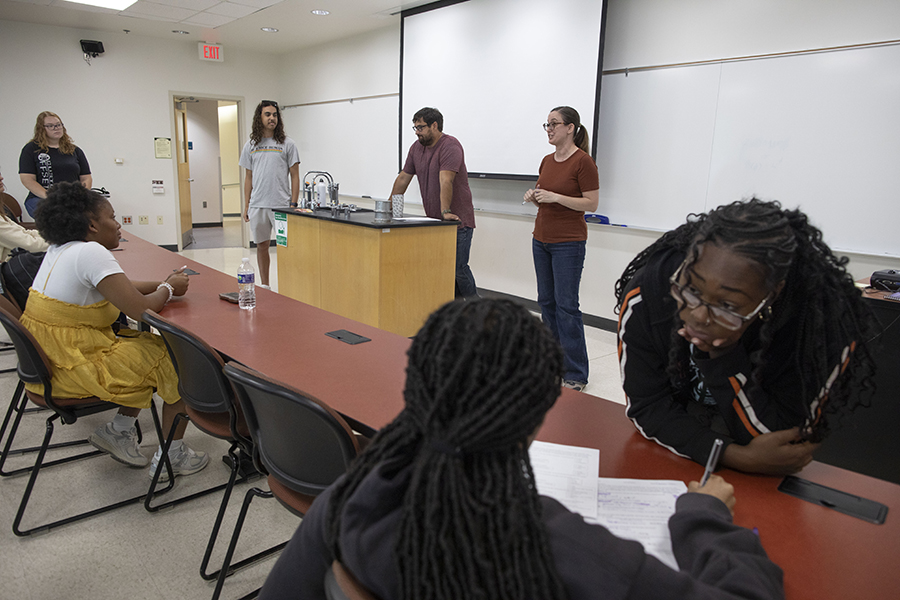 Anneke Lisberg speaks at the front of a class as students sit at red tables.