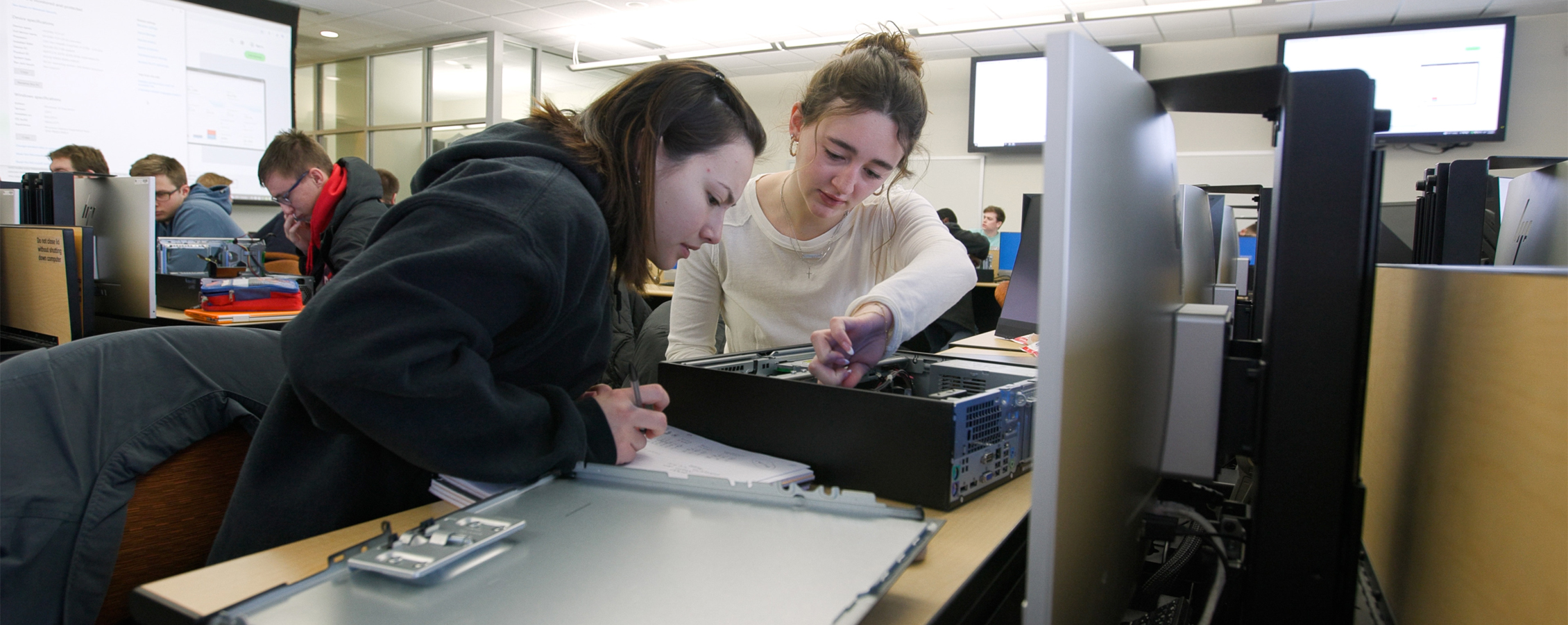 Two students work together as they take apart a desktop computer.