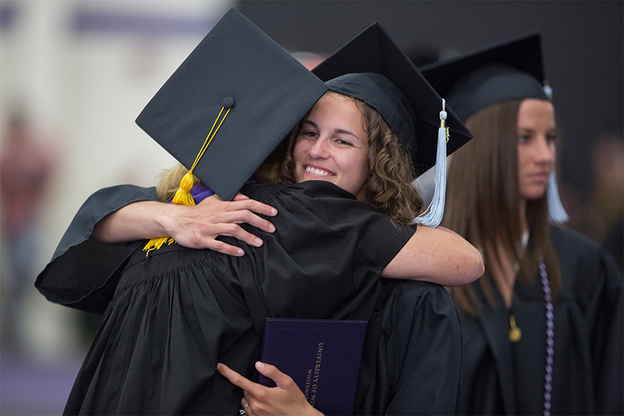 Kathleen Happel, left, hugs a student at graduation, both in cap and gown.