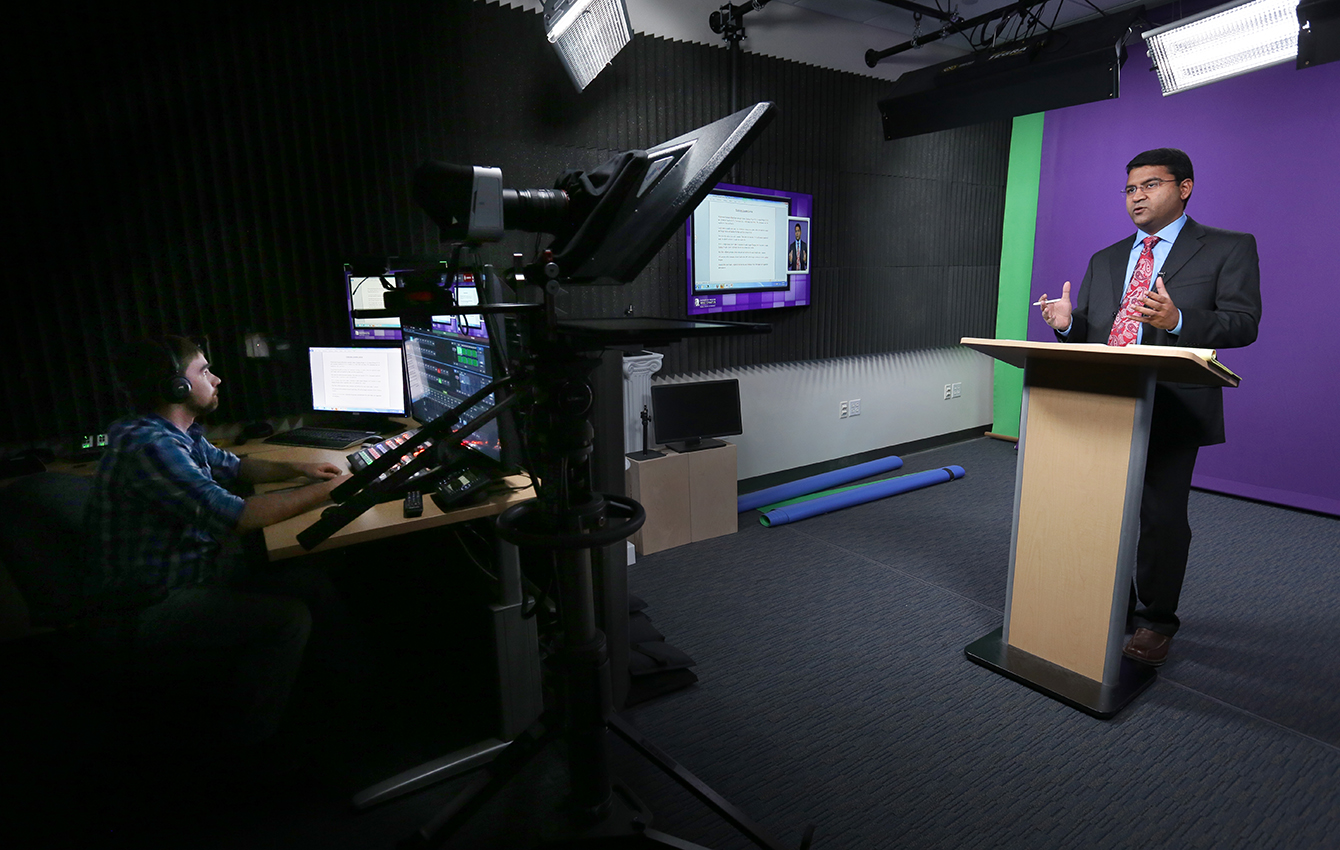 A person speaks at a podium while another video records him.