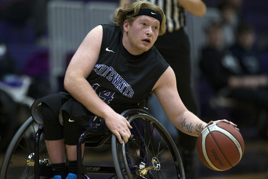 A wheelchair basketball player dribbles down the court.