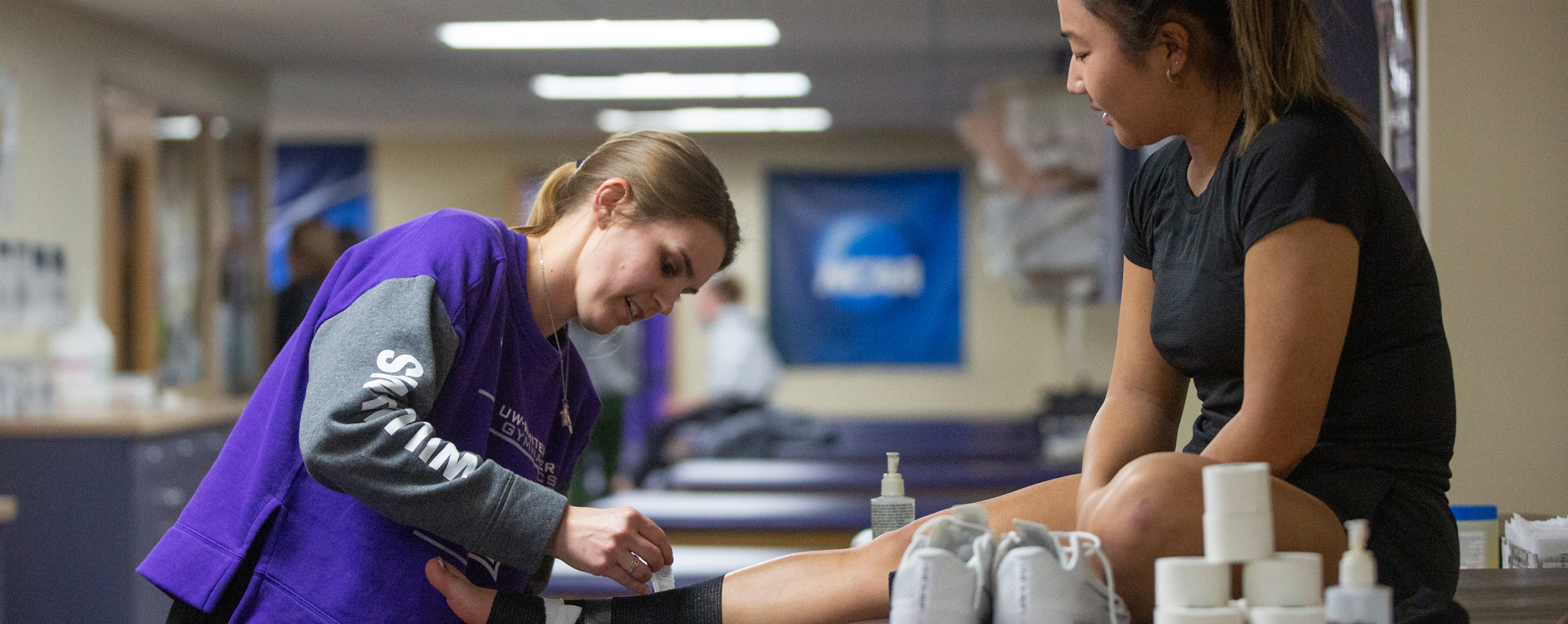 A trainer bandages a Warhawk athlete sitting on a table.
