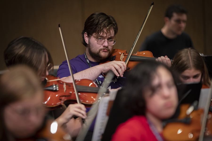 A student in a purple shirt plays a violin.
