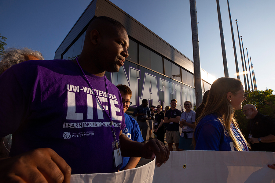 A person wearing a LIFE tshirt helps to hold a white banner.