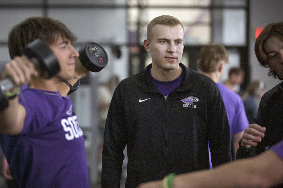 Ty Jahnke stands among other young men, one who is doing shoulder flys with dumbbells.