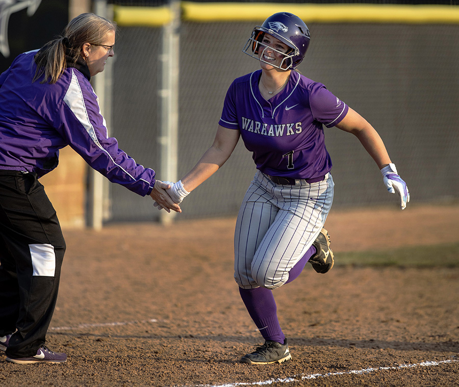 A Warhawk softball player rounds the bases as she low-fives her coach.
