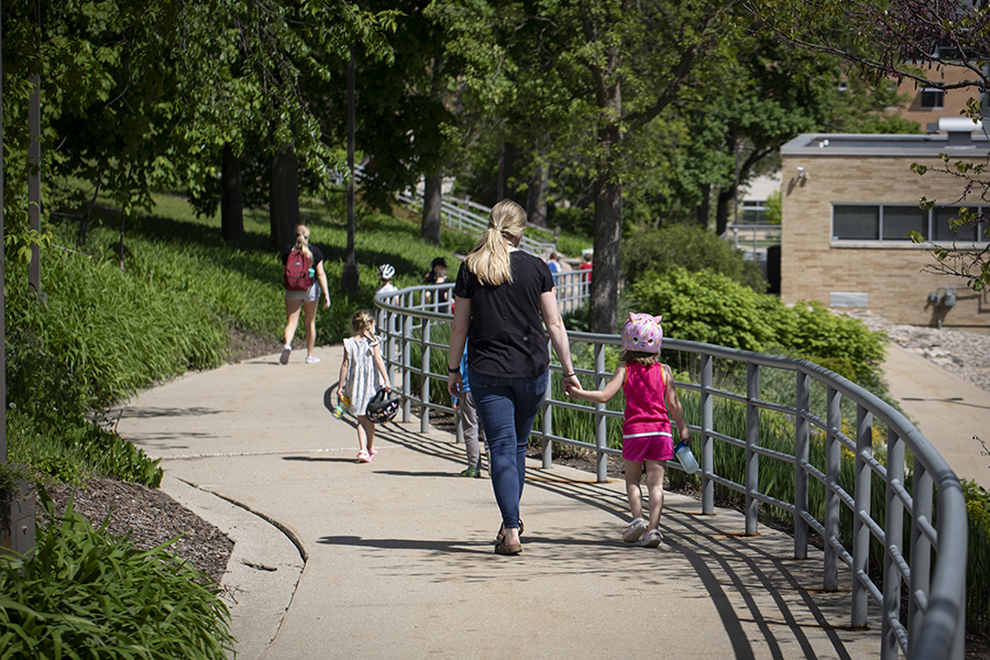 A teacher from the Children's Center holds hands with a child as they walk down a path on campus.