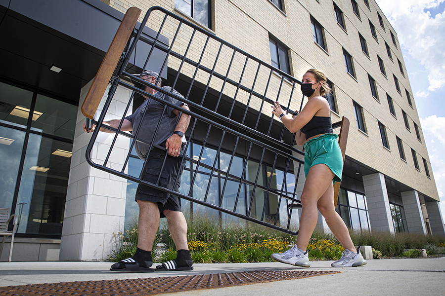 A student and her dad carry in the frame of a futon into a residence hall.