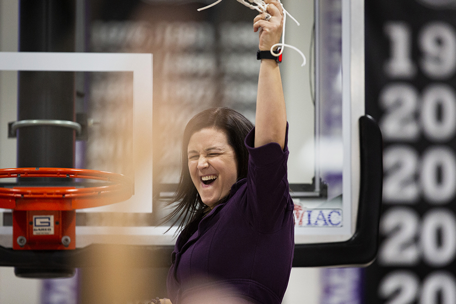 Keri Carollo stands on a ladder as she cuts part of the net from the basketball hoop in celebration.