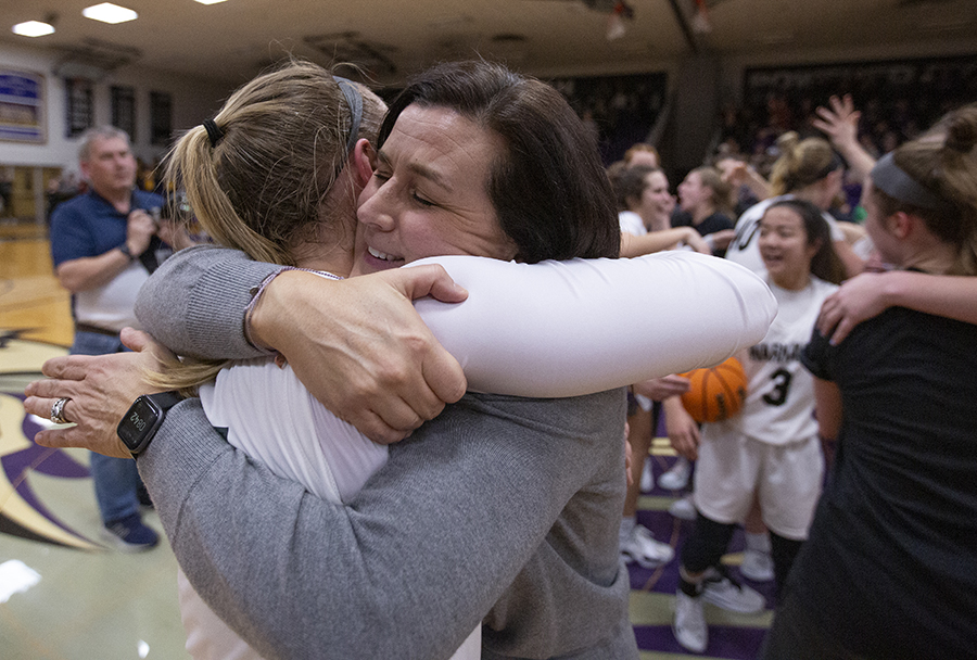 Keri Carollo hugs a player as they celebrate on the basketball court after a win.