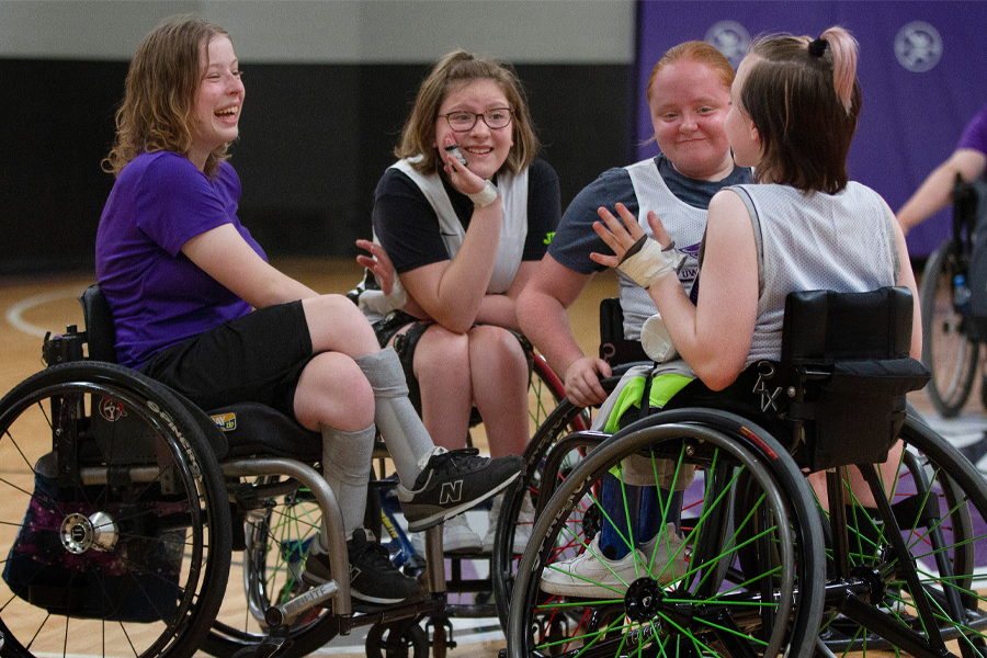 A group of young, female wheelchair basketball players huddle together on a basketball court.