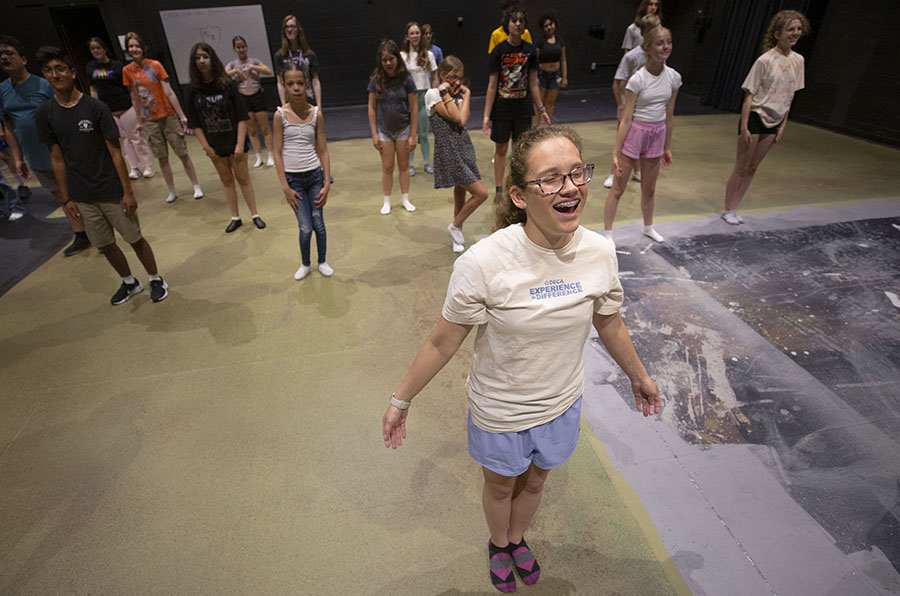 A camper stands at the front of class with her arms out and mouth open as she sings enthusiastically. 