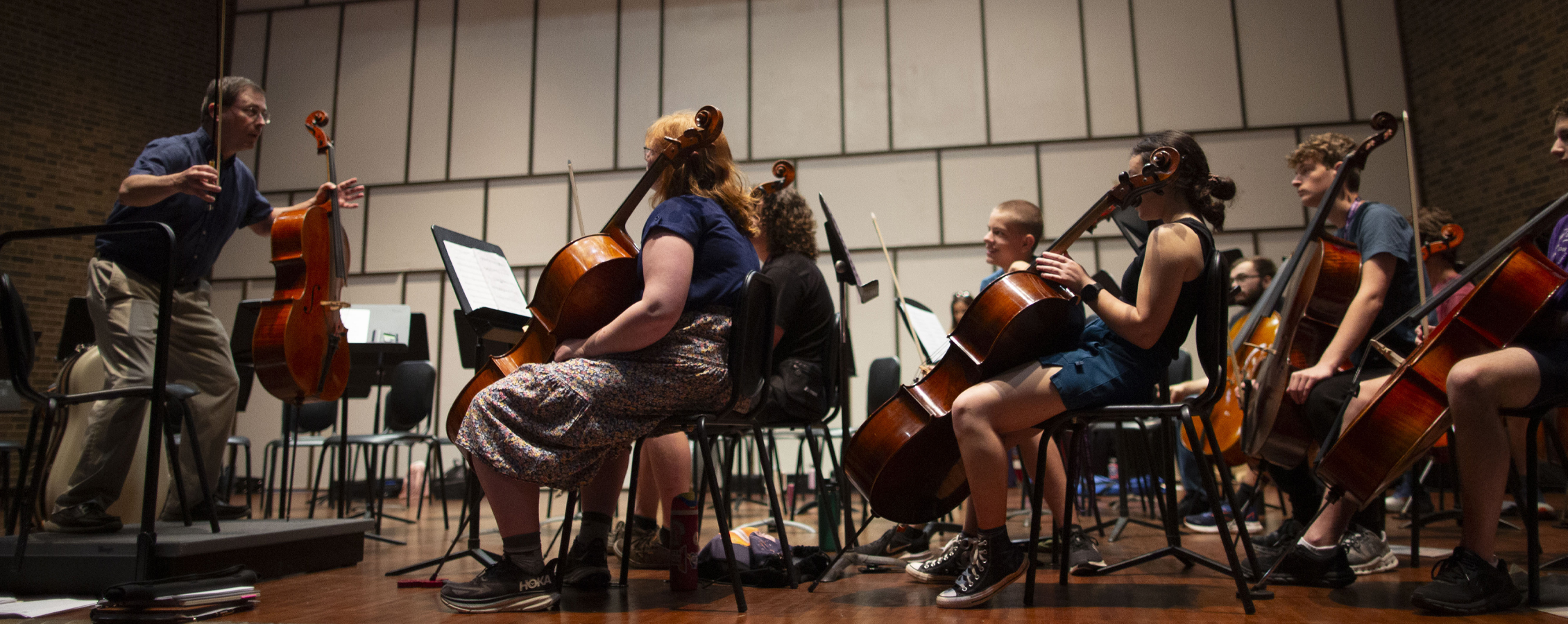 A faculty member stands in front of camp musicians who are sitting and large string instruments.