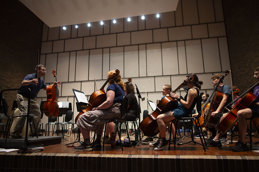 A faculty member stands in front of camp musicians who are sitting and large string instruments.