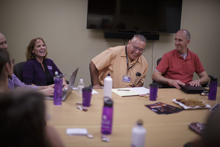 People sit around a table with purple water bottles on the table. 