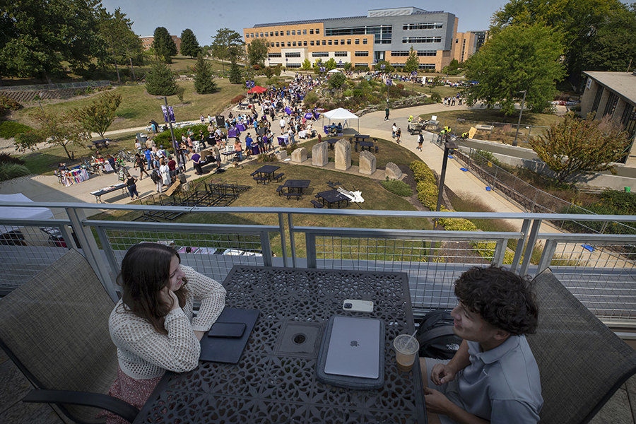 Students fill the sidewalks in the middle of campus with Hyland Hall in the background.