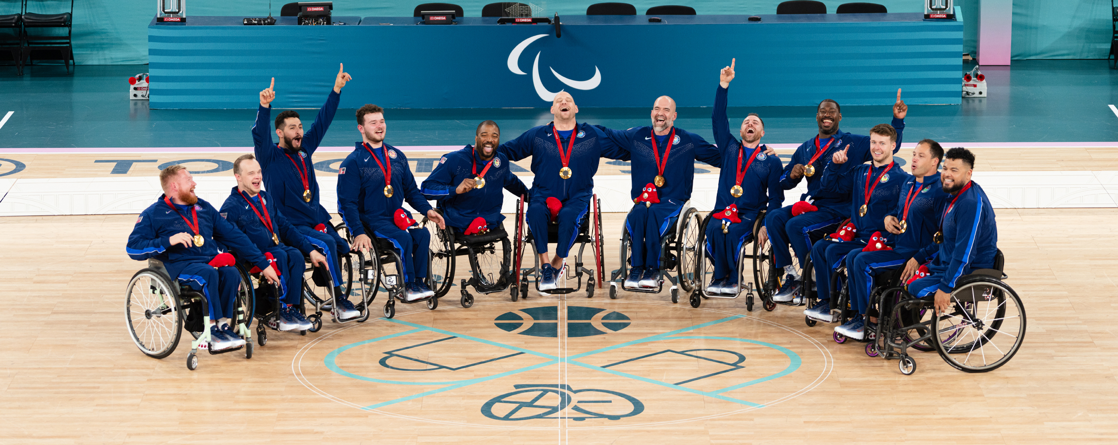 The men's Team USA gathers on the basketball court wearing gold medals.