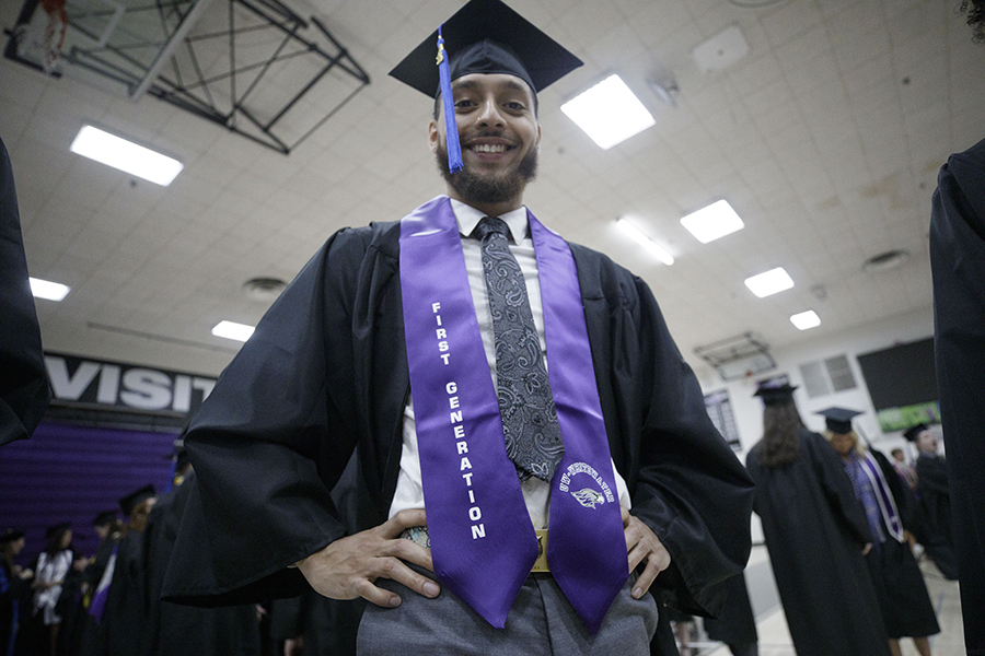 A student wearing academic regalia smiles at graduation.