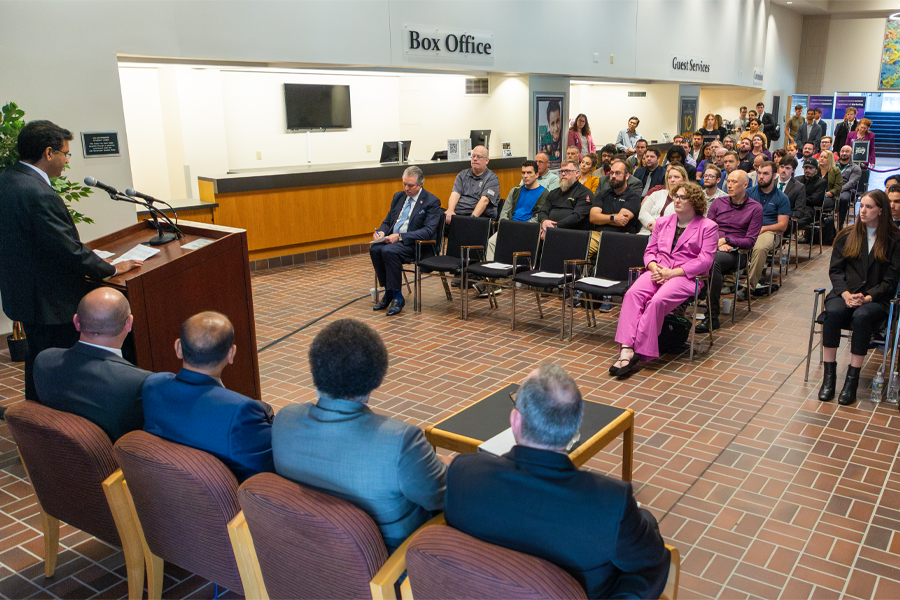 A faculty member speaks at the front of a crowd of people sitting in chairs. 