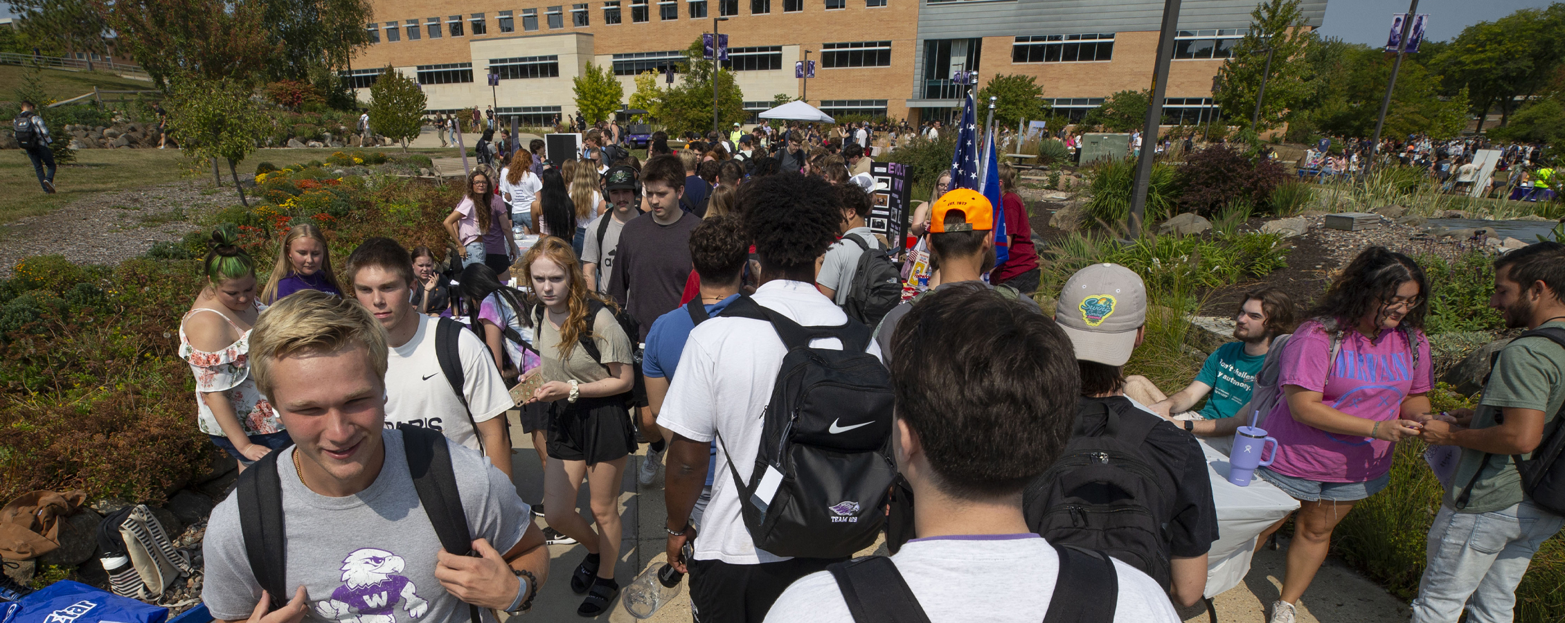 Students fill the sidewalks in the middle of campus with Hyland Hall in the background.