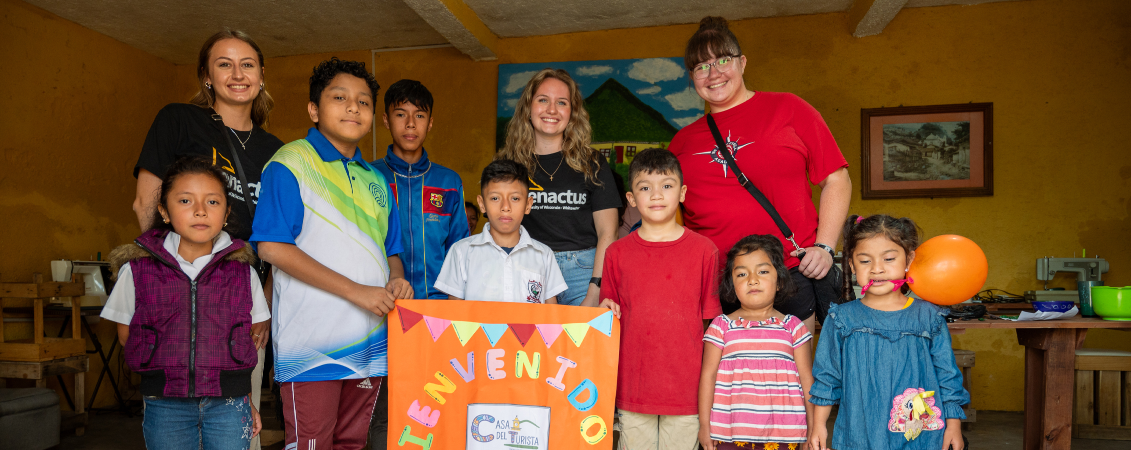 Three students stand with a group of Guatemala children who hold a colorful banner.