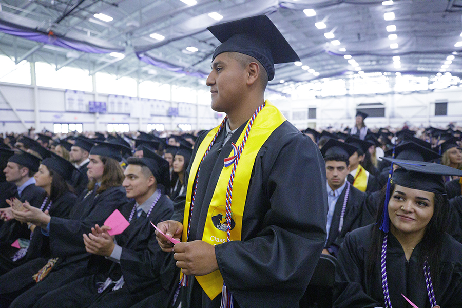 A group of graduates clap at commencement dressed in caps and gowns.