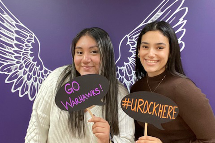 Alma Diaz-Cosme and Maribel Rodriguez pose for a photo and hold up signs that say go Warhawks and U Rock Here.