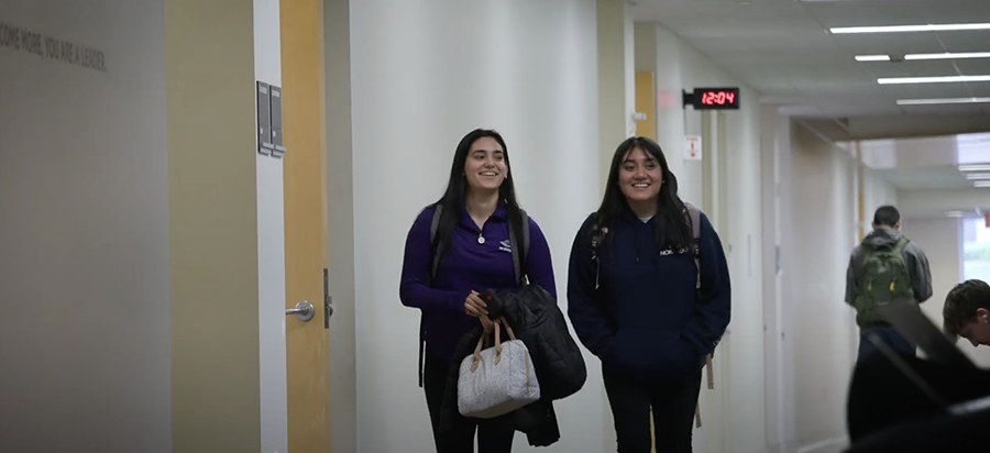 Alma Diaz-Cosme and Maribel Rodriguez walk down a hallway together.