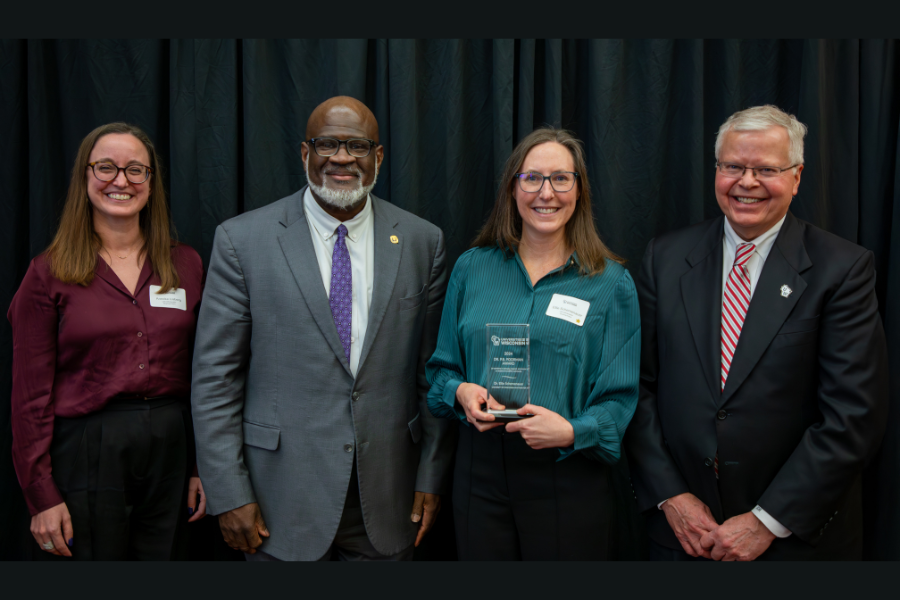 Ellie Schemenauer standing next to the chancellor and other staff members, holding award 