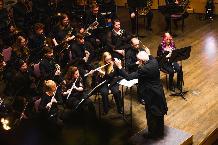 Glenn Hayes with arms raised as he conducts students playing instruments.