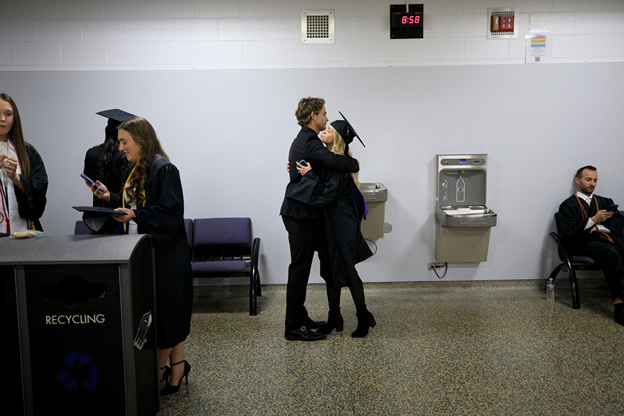 A couple hugs, one is wearing graduation regalia.