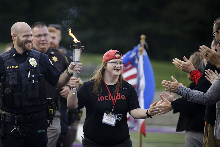 A special olympian runs through a crowd and receives high fives as they carry the ceremonial torch.